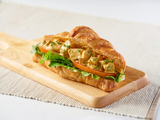 Curry Chicken Salad Croissant filled with lettuce and tomato slice on wooden cutting board side view of food menus