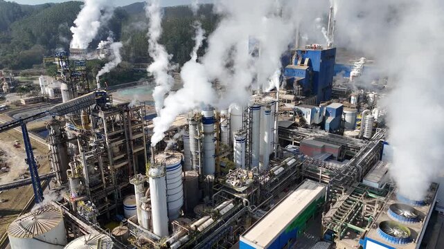Imagem a&eacute;rea de f&aacute;brica de papel e celulose com chamin&eacute;s e caldeiras, liberando poluentes vis&iacute;veis, mostrando os desafios ambientais e os efeitos da industrializa&ccedil;&atilde;o no ar e na paisagem