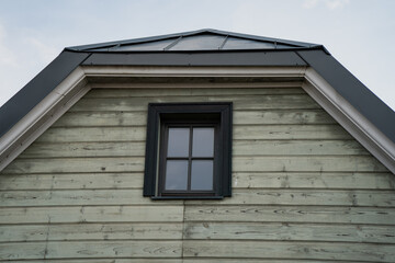 Traditional wooden house facade with small window and triangular roof design in rustic architecture style under cloudy sky captured in closeup detail