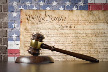 United States Constitution and American Flag On Wall with Gavel Resting on Table in Front.
