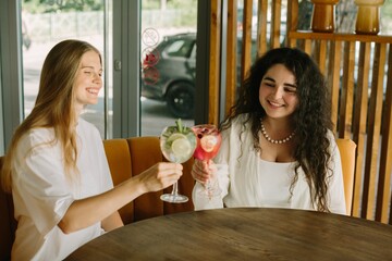 Two young women toasting with refreshing cocktails in a cafe