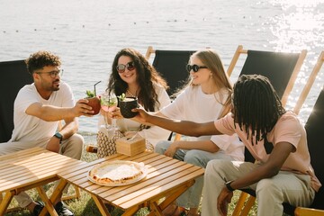 Cheerful friends toasting cocktails, enjoying lakeside vacation