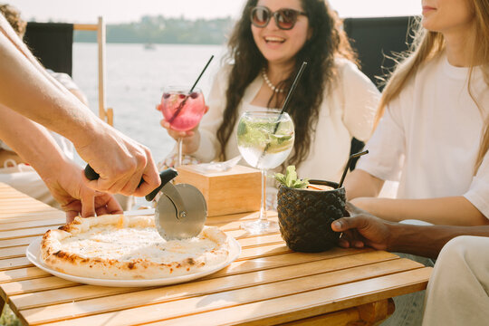 Waiter slicing pizza for friends enjoying drinks at outdoor cafe