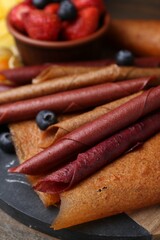 Delicious fruit leather rolls and berries on table, closeup