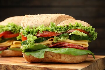Pieces of tasty baguette sandwich with smoked sausage, cheese and vegetables on wooden board against dark background, closeup