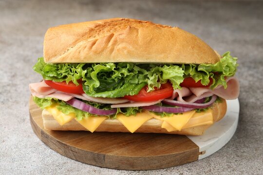 Tasty baguette sandwich with ham, cheese and vegetables on grey textured table, closeup
