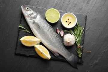 Fresh raw seabass with spices on black table, top view. Fish and seafood delicacies
