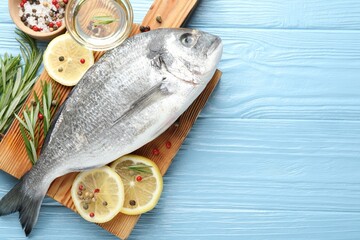 Fresh raw dourade fish with spices on blue wooden table, flat lay and space for text. Seafood delicacies