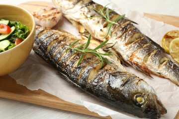 Tasty roasted seabass fish served with salad and lemon on white wooden table, closeup. Homemade...