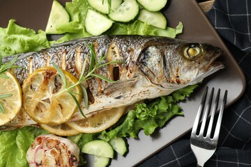 Tasty roasted seabass fish served with vegetables and lemon on table, flat lay. Homemade seafood dish