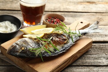 Tasty roasted dorado fish served with rosemary and lemon on wooden table, closeup. Homemade seafood...