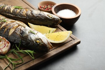 Tasty roasted seabass fish served with rosemary and lemon on grey table, closeup and space for text. Homemade seafood dish