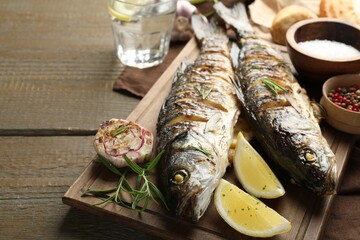 Tasty roasted seabass fish served with rosemary and lemon on wooden table, closeup. Homemade seafood dish