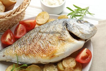 Tasty roasted dorado fish served with vegetables and sauce on white wooden table, closeup. Homemade seafood dish