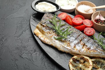 Homemade seafood dish. Tasty roasted mackerel served with spices and sauce on black table, above view. Space for text