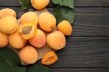Fresh apricots and green leaves on dark wooden table, flat lay. Space for text