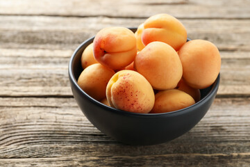 Fresh apricots in bowl on wooden table, closeup