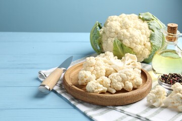 Pieces of cauliflower, peppercorns, oil and knife on light blue wooden table. Space for text