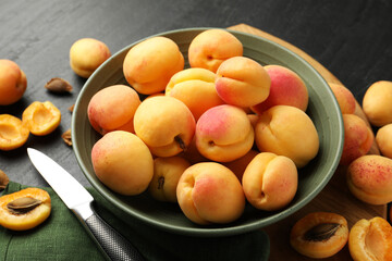 Fresh ripe apricots in bowl and knife on black table, closeup