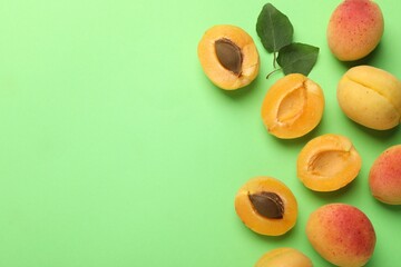 Fresh ripe apricots and leaves on green background, flat lay. Space for text