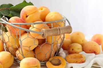 Fresh ripe apricots in metal basket and green leaves on table, closeup