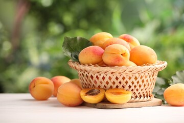 Fresh ripe apricots in wicker basket on white wooden table outdoors