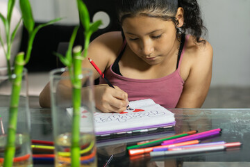 Young Latina girl focused on coloring hand-lettered design in her notebook at home