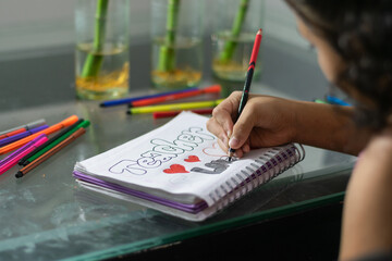 close up of girl’s hand coloring stylized letters in her notebook with markers