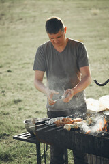 Grilling Meat Skewers on a Charcoal Barbecue with Smoke and a Man Outdoors