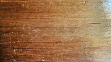 A close-up of a wooden surface with a warm, brown tone and visible wood grain, featuring horizontal lines and subtle imperfections.