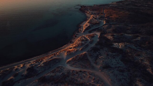 Drone view of a Sea of Cortez beach during golden hour, where the shoreline glows in gold and soft pink hues while crystal-clear water reflects the stunning colors of sunset.