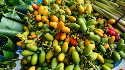 Melinjo fruits in a vibrant array of green, yellow, and red hues are bundled, with some wrapped in green leaves.