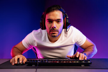 Smart gaming streamer looking at camera with trendy pose, passing the level of online game user on pc, using headset and mic for communicate with others at digital neon light studio room. Surmise.
