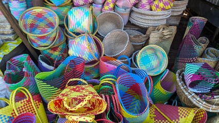 A vibrant display of colorful woven baskets or bakul. The items showcase a variety of shapes, sizes, and patterns, creating an eye-catching and artistic arrangement.