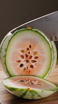 Close Up of Fresh Whole Watermelon Being Sliced with Sharp Knife on Wooden Surface Under Studio Lighting