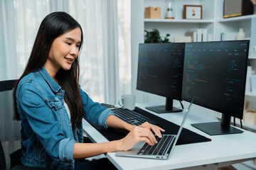 Smiling young Asian in IT developer creating with typing online information on laptop with coding...