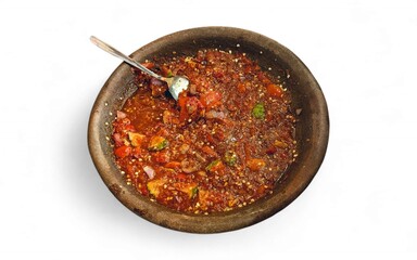 A bowl of Indonesian sambal with a spoon on a white background. The sambal appears rich and spicy, showcasing vibrant colors and textures.