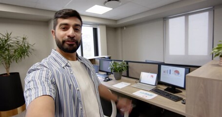 Pointing Indian man gesturing toward laptop, monitors and printed charts at office desk, copy space - Powered by Adobe