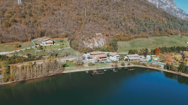 Drone shot of Lake Idro with hillside homes, autumn trees, green meadows, and blue water