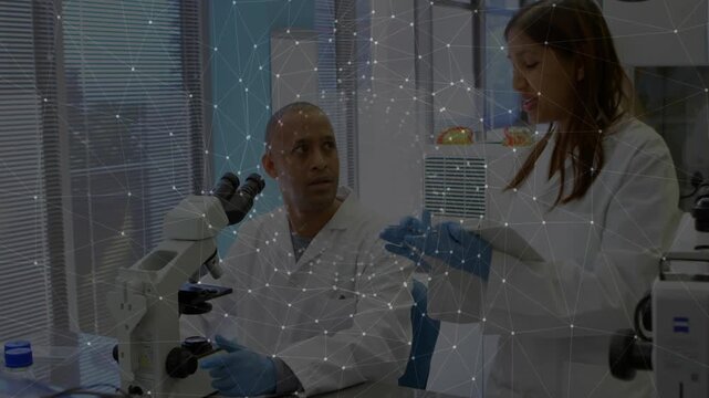 Male scientist examining lab slide, colleague entering with vial tapping tablet explaining size