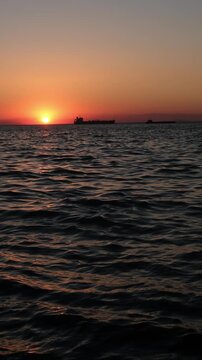 Cargo ships silhouettes at sunset with ocean waves in 4K. Commercial vessels on calm sea at dramatic sunset.