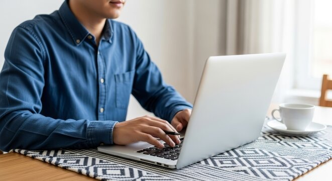 Focused man typing on laptop at a table with coffee.