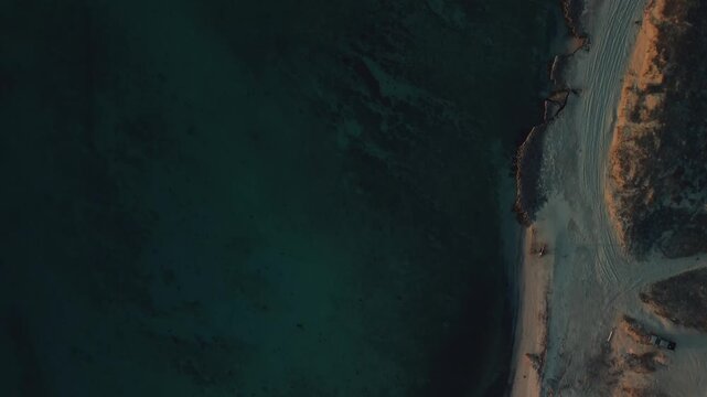 Top-down drone view of the Sea of Cortez at sunset near El Tecolote Beach, revealing crystal-clear turquoise water, visible seabed, golden shoreline, and breathtaking coastal scenery bathed in warm ev