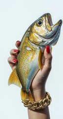 A hand with red nails and a gold bracelet holds a shiny golden fish upright against a light background, blending fashion, nature, and contrast in a bold, surreal composition.