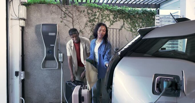 African American couple approaching carport stowing luggage in EV trunk unplugging charger, leaving