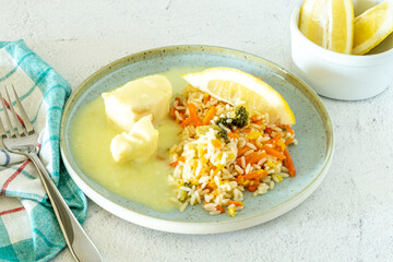Cod fish meal filet on lemon sauce with vegetable rice in plate on white marble