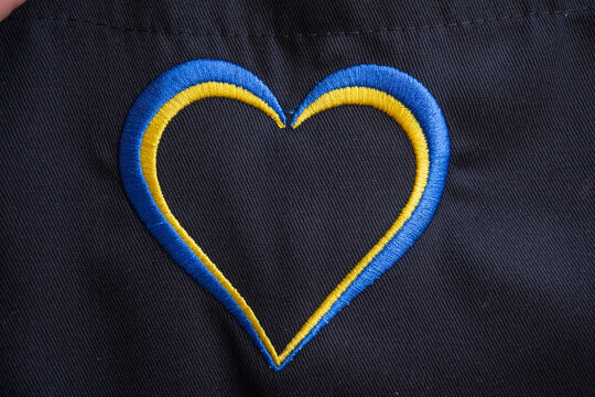 un corazón bordado con hilos de color azul y amarillo con fondo negro - Powered by Adobe