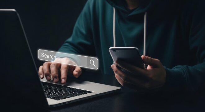 A person is searching the internet on a laptop while using a mobile phone