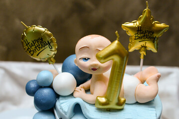 A two-tiered black and blue birthday cake with a baby on top and decorated with baby motifs