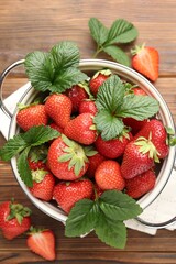 Fresh ripe strawberries and leaves in metal colander on wooden table, flat lay